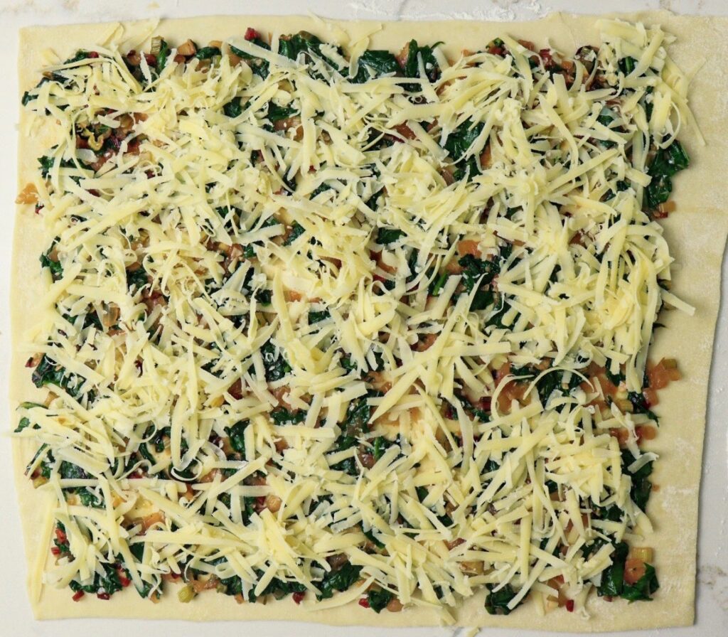 Swiss chard filling topped with Gruyère on puff pastry sheet