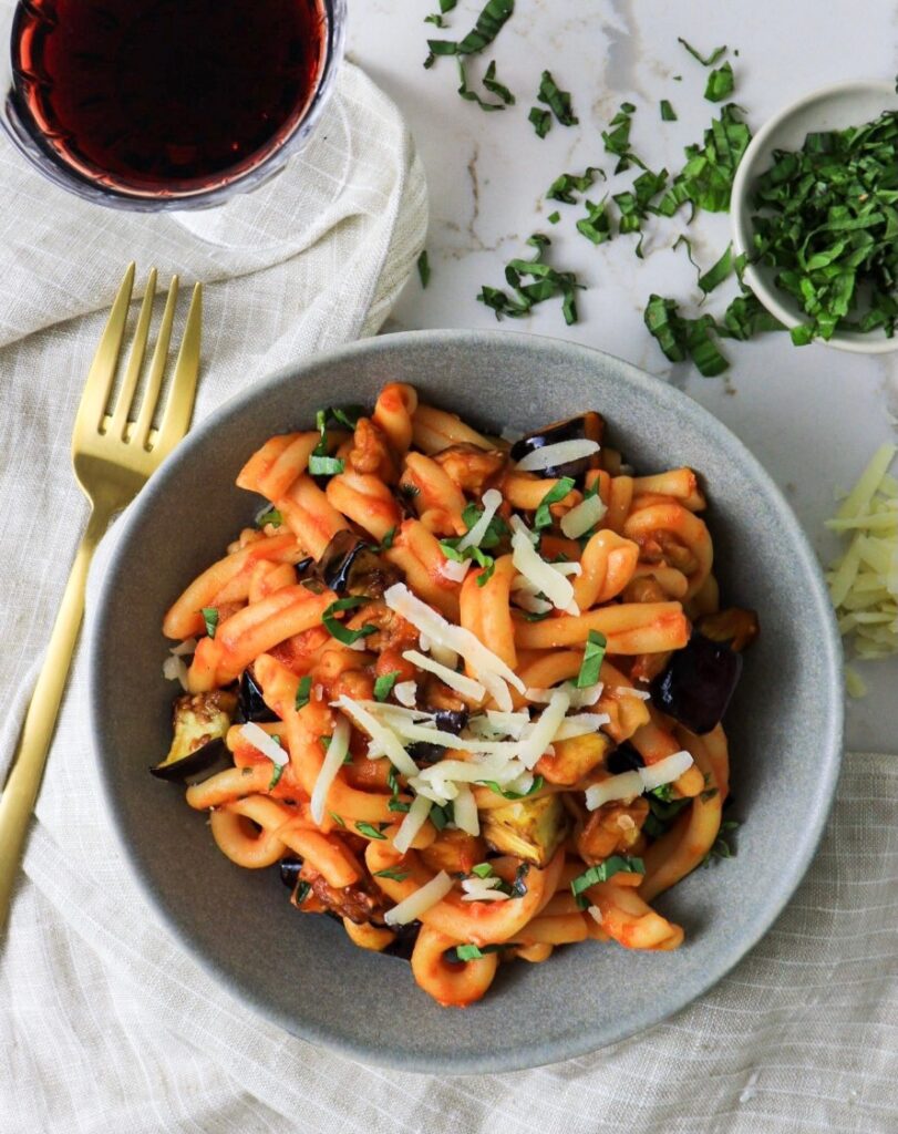 Bowl of pasta alla norma with glass of wine